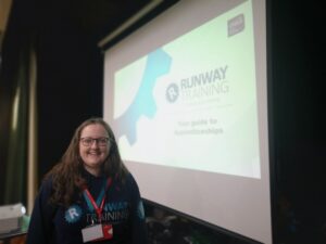 Rebecca from Runway Training, stood in front of the company's logo on a projector screen. 